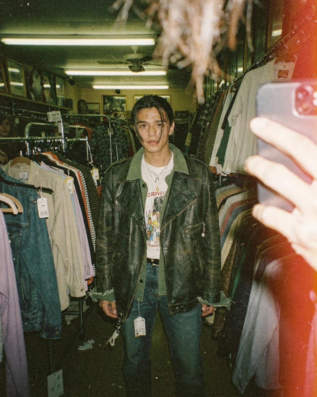 Thrift store mirror selfie in disposable-camera style, showing a shopper evaluating outfit fit before purchase and virtual try-on confidence