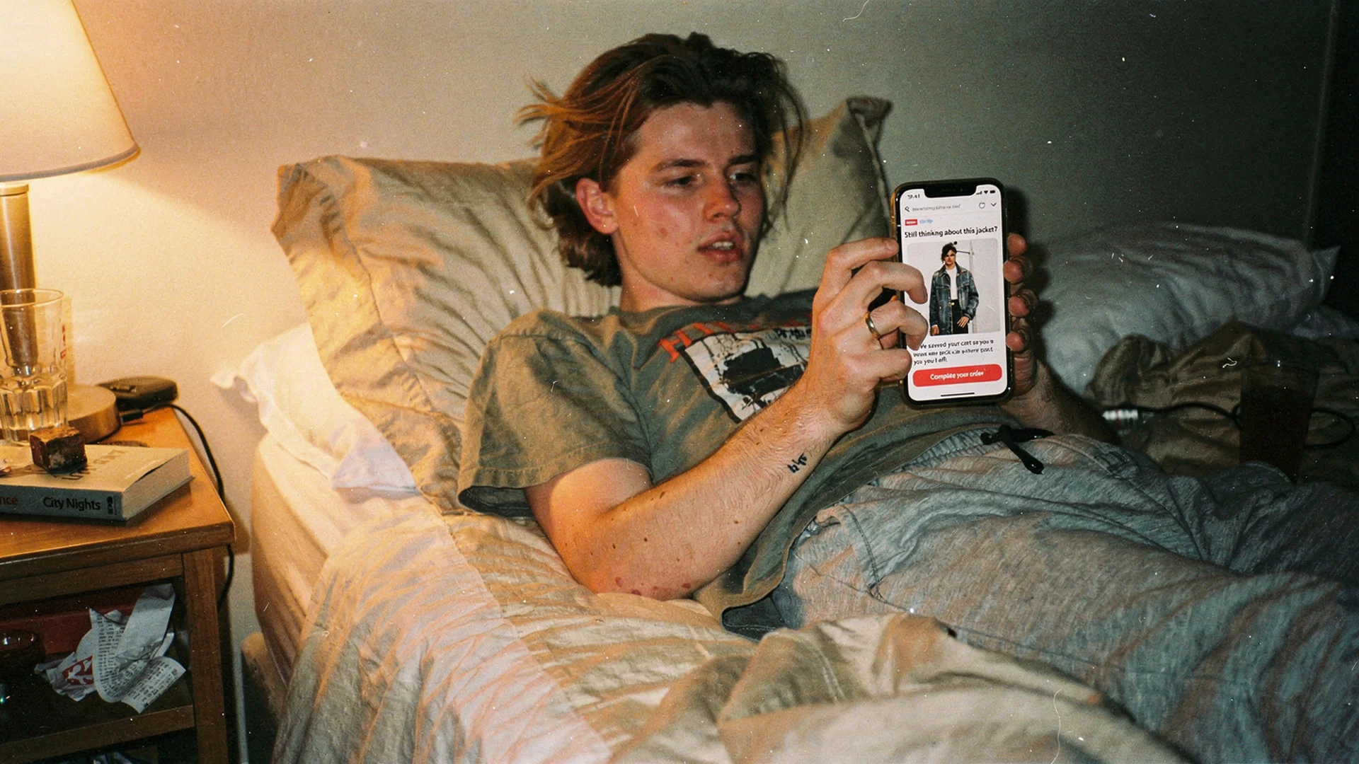 Disposable-camera style photo of a phone on a kitchen table showing a fashion cart reminder email mid-tap